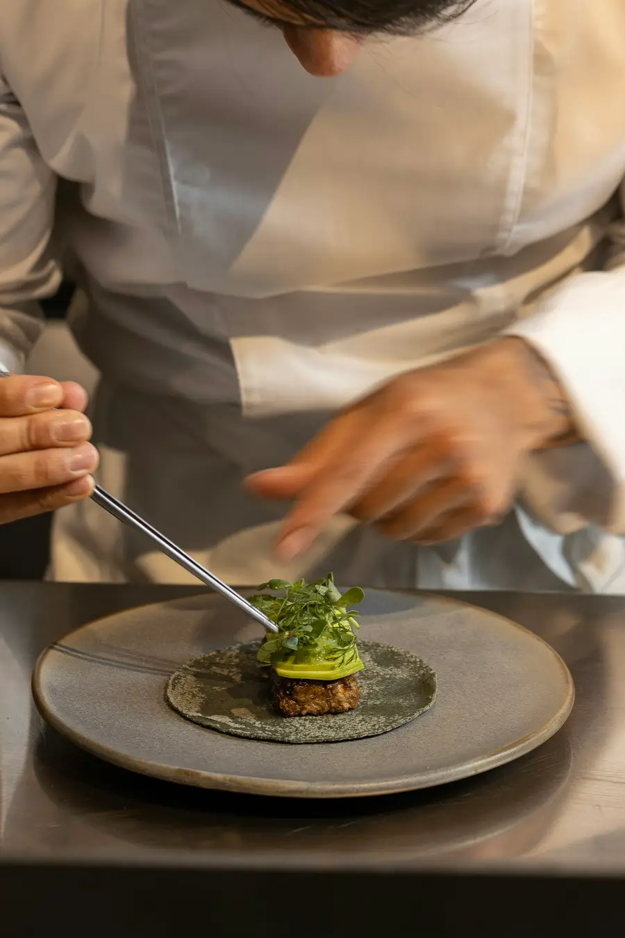 Las manos de la chef terminan un plato con pinzas