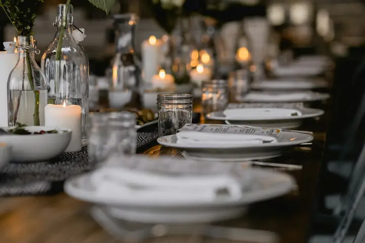 Mesa larga con platos blancos, velas y botellas de cristal