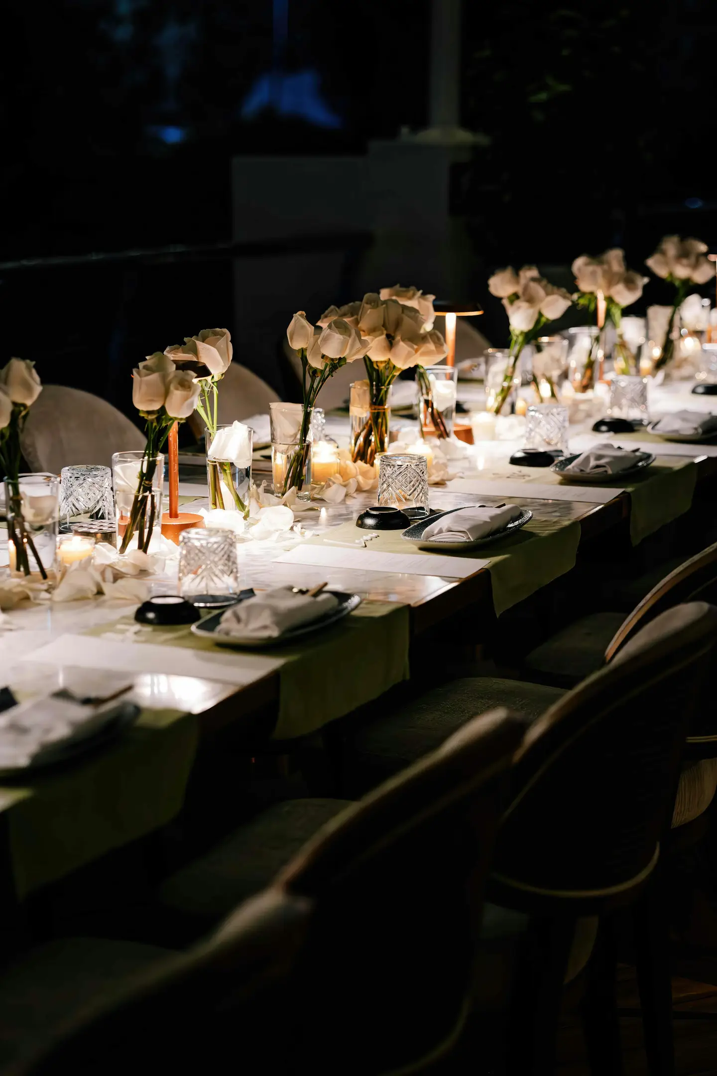 Mesa larga vestida con velas y flores en una sala en penumbra